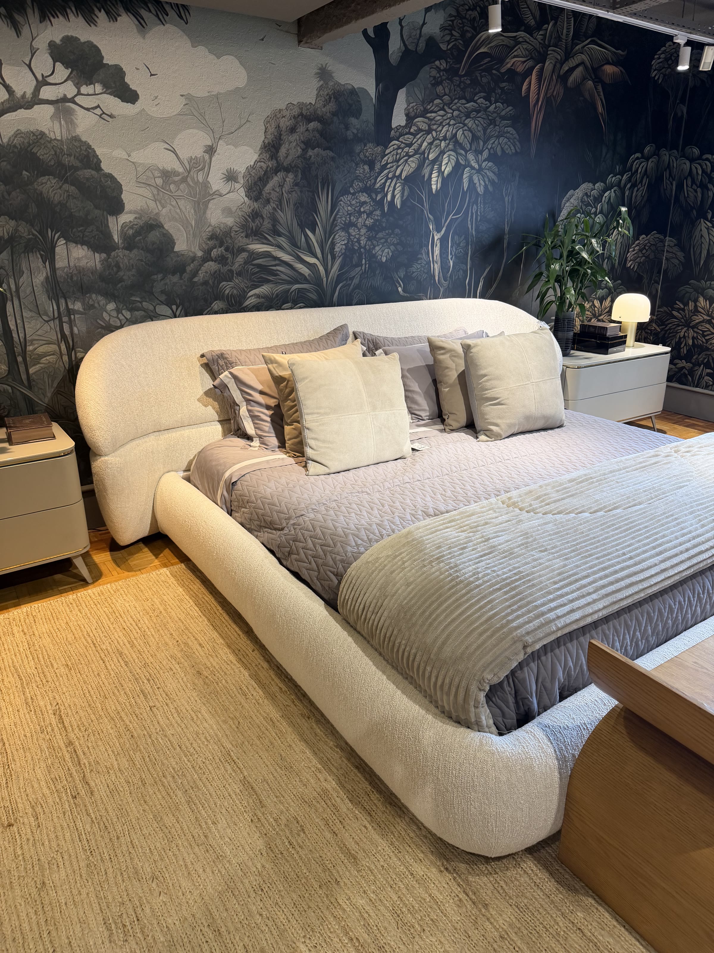 Dormitório de showroom com cama estofada clara e painel botânico